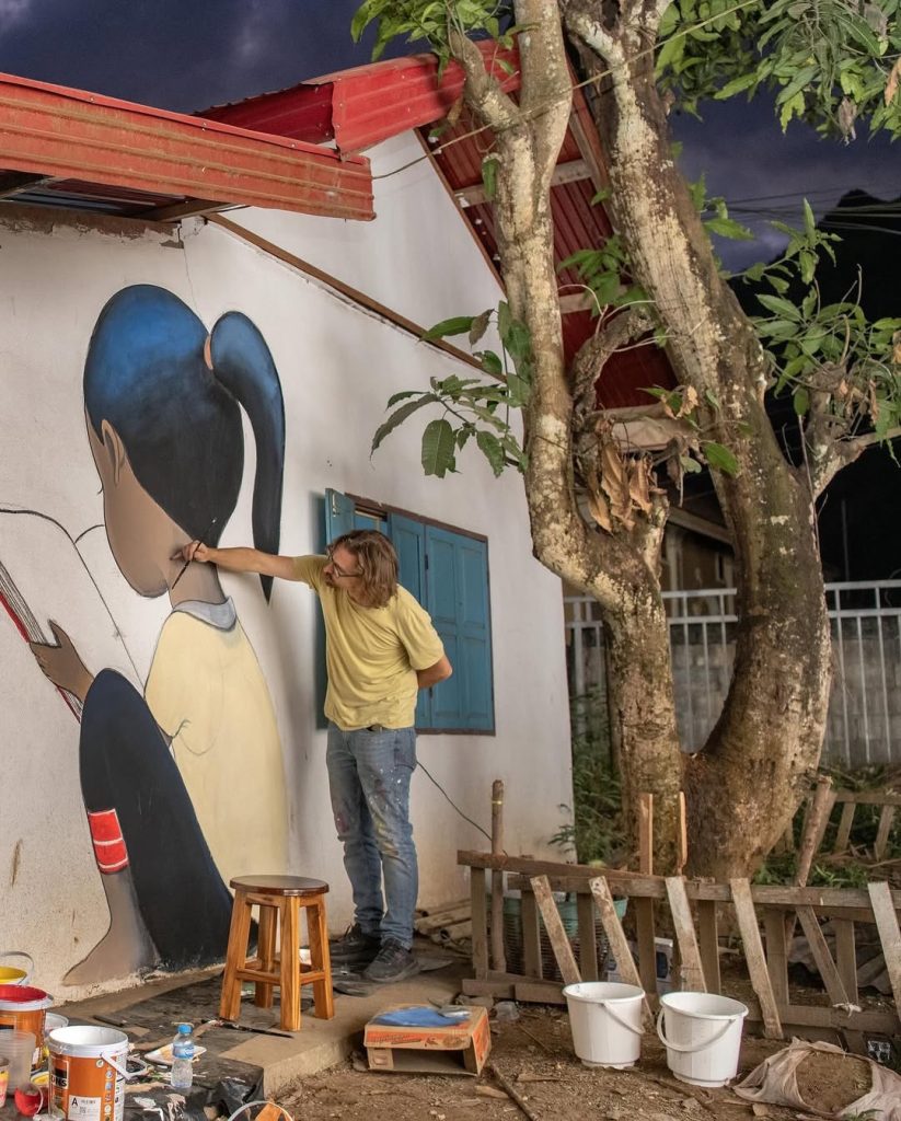 Seth Globepainter painting Tree of Books mural in Nong Khiaw
