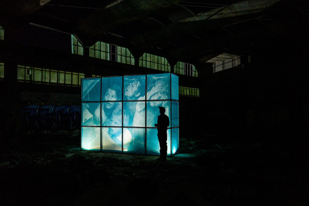 Ricardo Romero’s THE WORLD BURNS WHILE WE SCROLL, an illuminated installation of painting screens inside a dark industrial space.